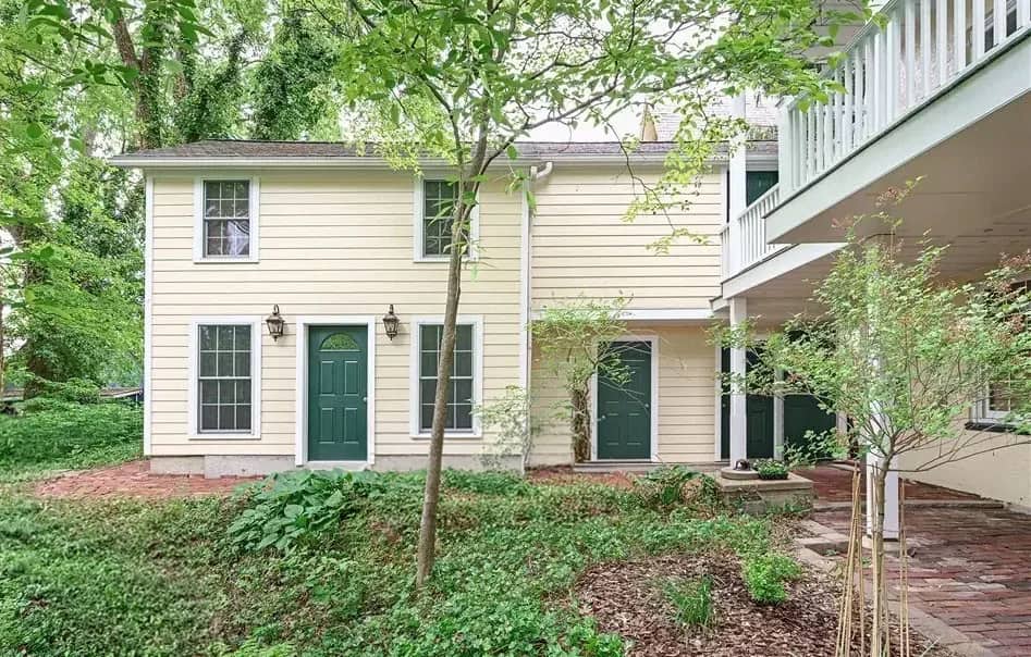 Daylight view of the restored carriage house beside the main house, surrounded by mature trees and garden plantings