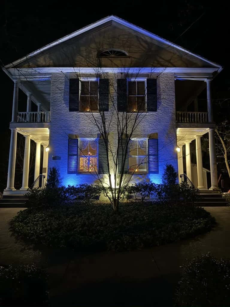 The white Greek Revival facade illuminated in blue at night