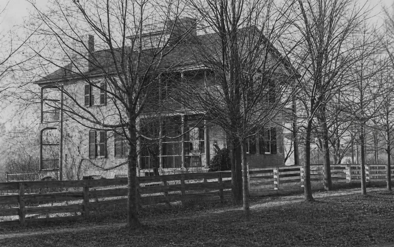 Restored nineteenth-century photograph of the House of Seven Porches behind a wooden fence and leafless trees
